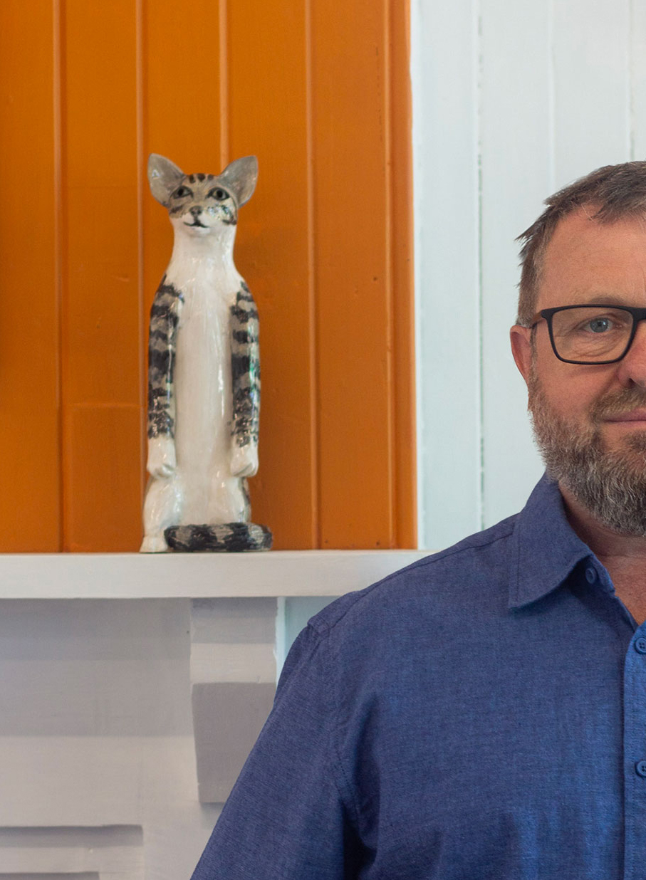 Mark Rayner standing in Space Studio Gallery with a ceramic cat on a shelf behind him